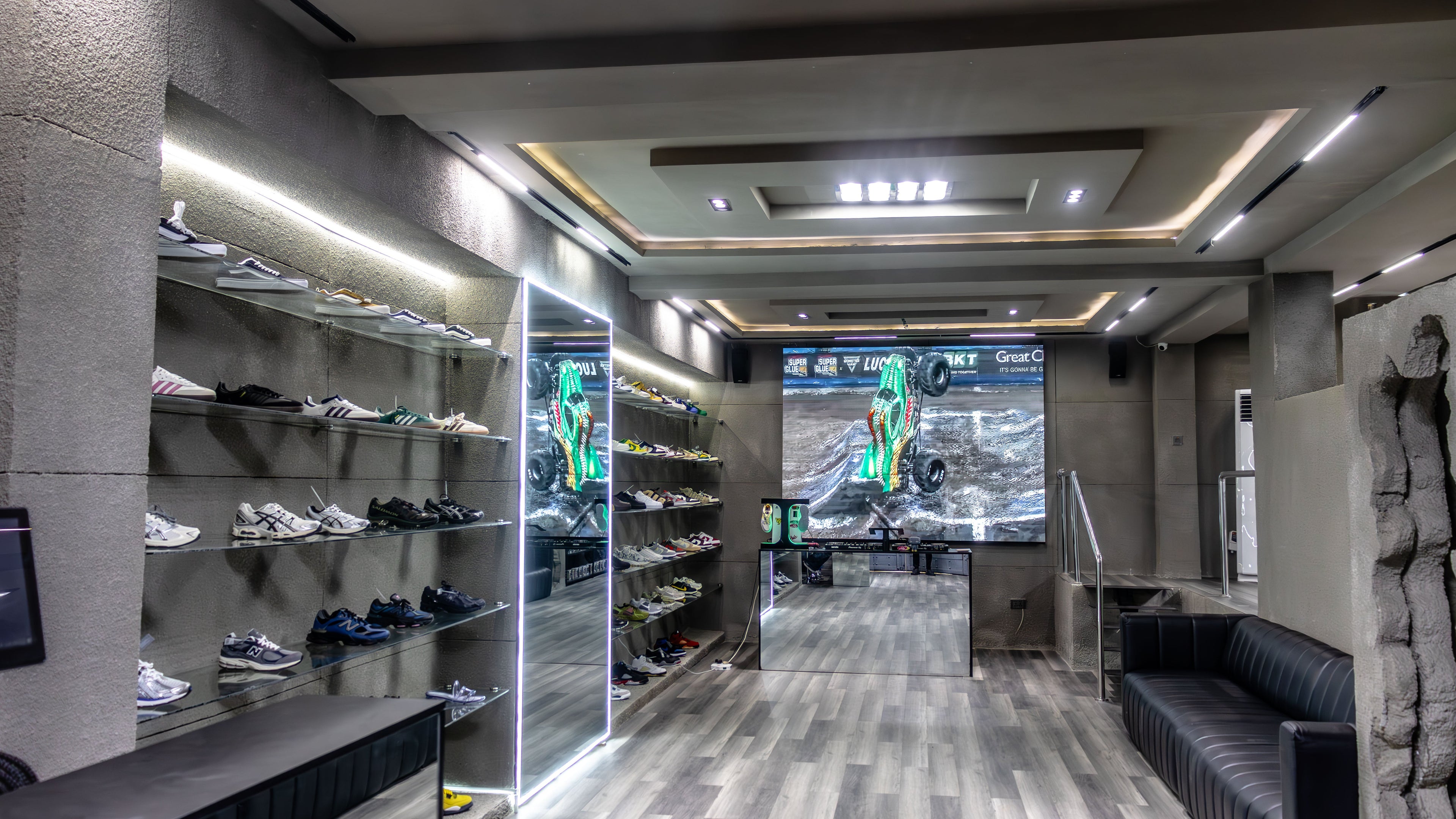 Modern home entertainment room with a large screen displaying a sports game, surrounded by shelves with shoes and a sofa.